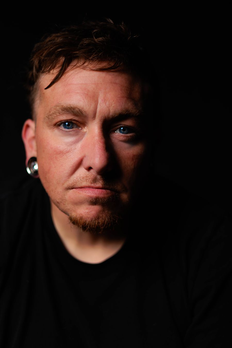 Portrait of Tyler Heath, photographer, lit from one side against a black background